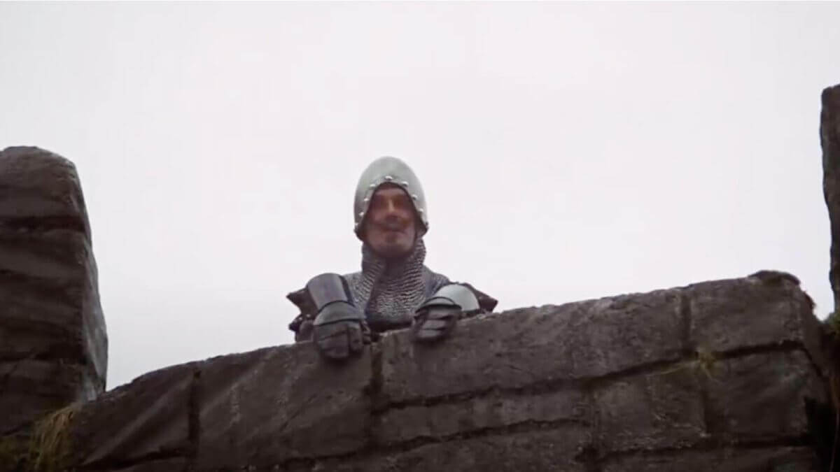 A castle guard peers over a stone wall — a still from Monty Python and the Holy Grail